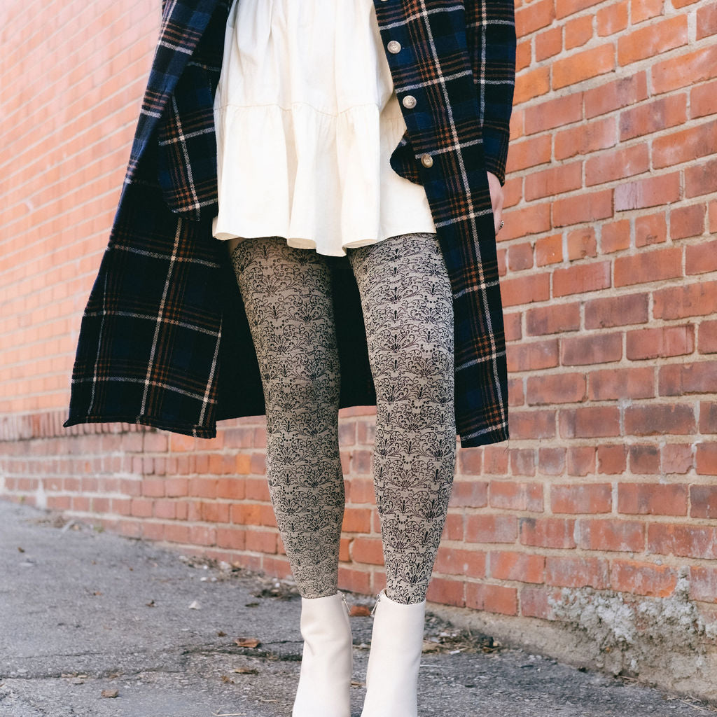 Legs in cream scroll-pattern tights and white boots by a brick wall