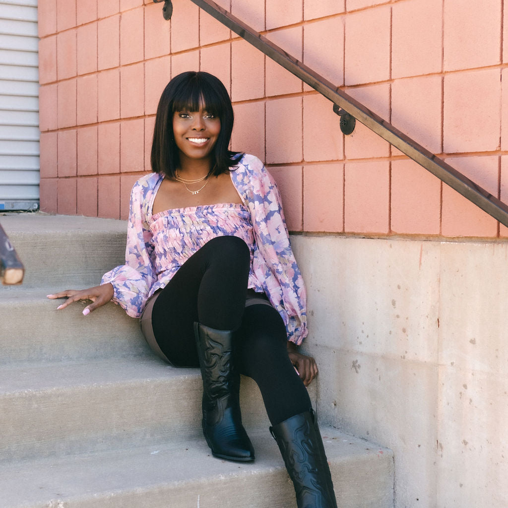 Woman sitting on steps in opaque black tights and boots
