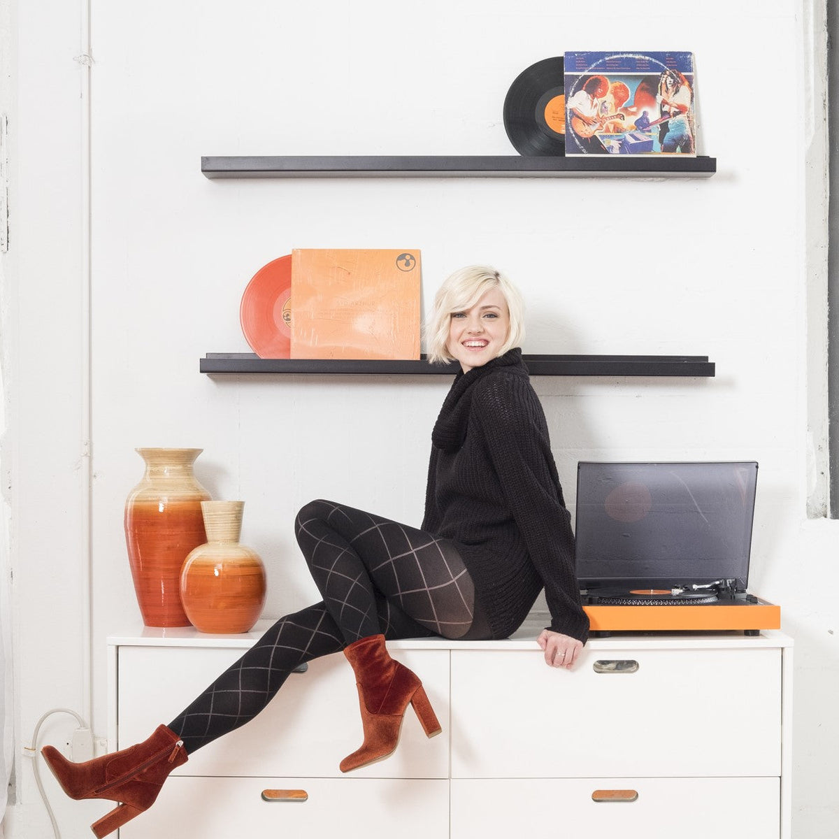 Smiling woman sitting on a white cabinet in diamond-pattern black tights