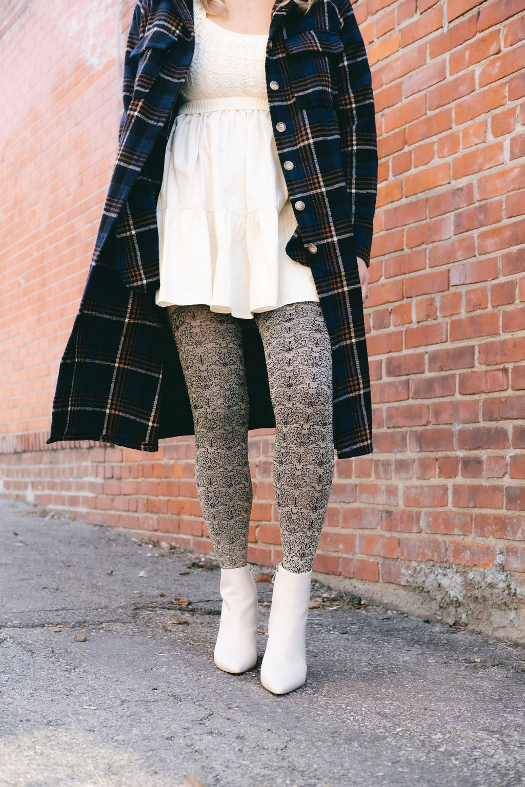 Legs in cream scroll-pattern tights and white boots by a brick wall